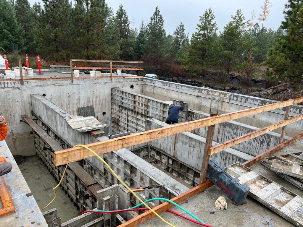Construction site with wooden forms for concrete foundation work, set amidst a forested area.